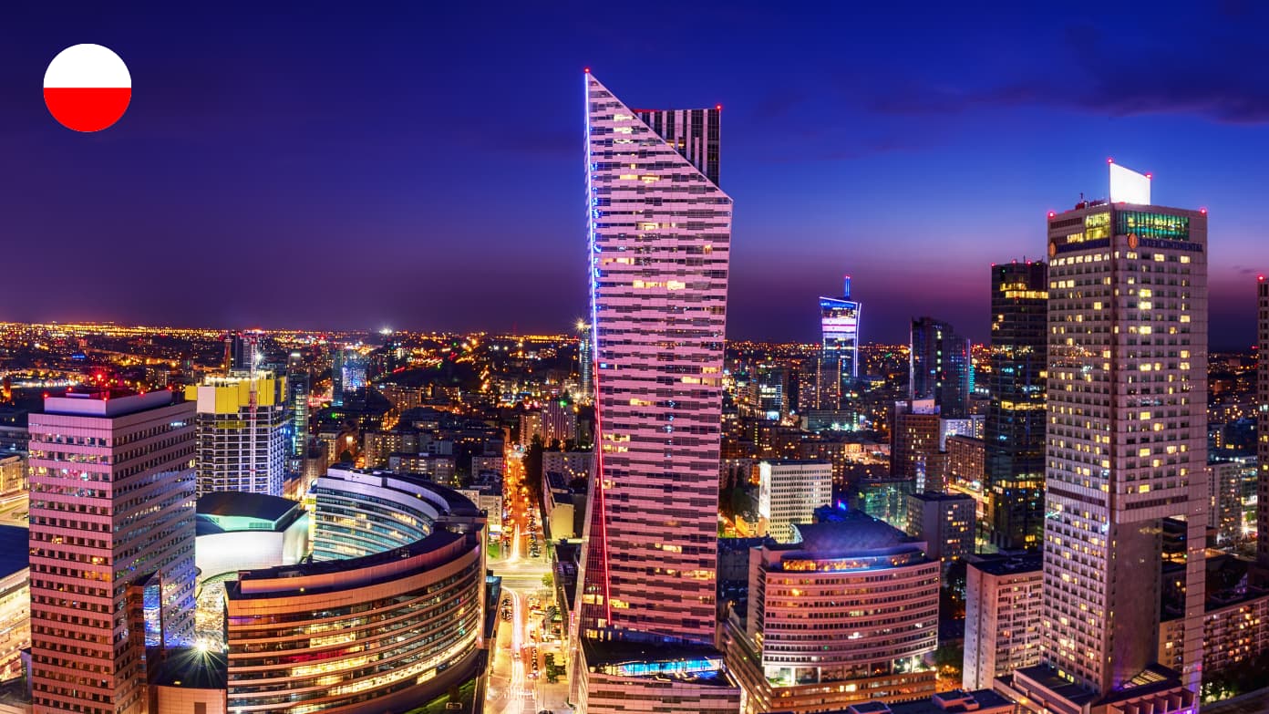 Illuminated skyscrapers of the Warsaw skyline at night with a small Polish flag icon in the top-left corner.​​ 
