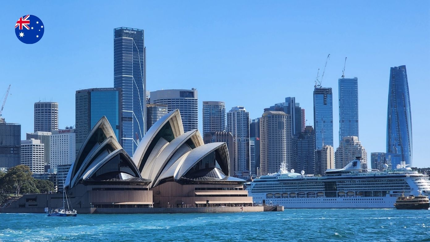 The Sydney Opera House on the harbor with the city skyline and a large cruise ship in the background​​ 
